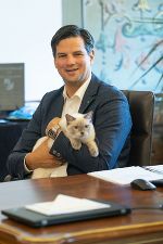 Bildbeschreibung: Person mit dunklem Anzug sitzt am Schreibtisch mit Katze.